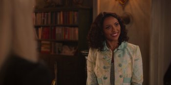 Movie still from “Love in the Villa” (2022), directed by Mark Steven Johnson – A woman smiling for the camera in front of bookshelves; Close Up shot, Over the shoulder angle