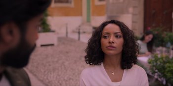 Movie still from “Love in the Villa” (2022), directed by Mark Steven Johnson – A woman standing on a sidewalk with a building in the background; Close Up shot, Over the shoulder angle