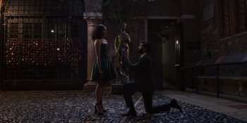 Movie still from “Love in the Villa” (2022), directed by Mark Steven Johnson – A man kneeling down to propose to a woman in front of a statue; Wide shot, High angle