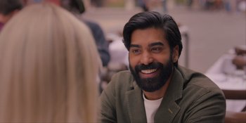 Movie still from “Love in the Villa” (2022), directed by Mark Steven Johnson – A man with long hair and a beard smiling for the camera; Close Up shot, Over the shoulder angle