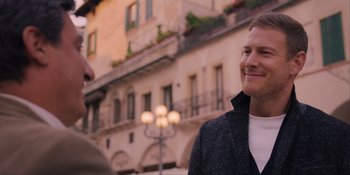 Movie still from “Love in the Villa” (2022), directed by Mark Steven Johnson – A man standing next to another man on a city street; Close Up shot, Over the shoulder angle