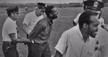 A black and white photo of a man being held by a police officer