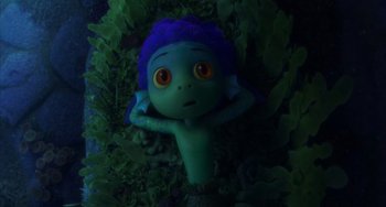 Movie still from “Luca” (2021), directed by Enrico Casarosa – A green doll with a blue wig laying in a bed of green leaves; Medium shot, High angle