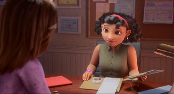 Movie still from “Luck” (2022), directed by Peggy Holmes – A woman sitting at a table with a picture of a girl; Medium shot, Over the shoulder angle