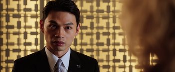 Movie still from “Lucy” (2014), directed by Luc Besson – A man wearing a suit and tie standing in front of a wall; Close Up shot, Low angle