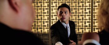 Movie still from “Lucy” (2014), directed by Luc Besson – A man wearing a suit and tie holding a pen; Close Up shot, Over the shoulder angle