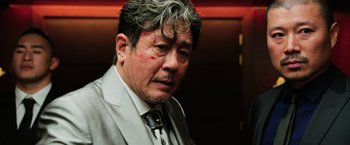 Movie still from “Lucy” (2014), directed by Luc Besson – An older asian man wearing a suit and tie; Close Up shot, Low angle