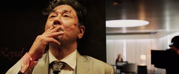 Movie still from “Lucy” (2014), directed by Luc Besson – A man in a suit and tie smoking a cigarette; Close Up shot, Low angle