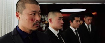 Movie still from “Lucy” (2014), directed by Luc Besson – A group of men in business suits standing next to each other; Close Up shot, Over the shoulder angle