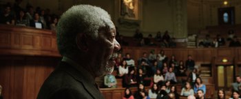 Movie still from “Lucy” (2014), directed by Luc Besson – An older man speaking in front of an audience; Close Up shot, High angle