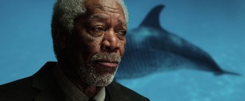 Movie still from “Lucy” (2014), directed by Luc Besson – An older man in a suit and tie with a shark in the background; Close Up shot, Low angle