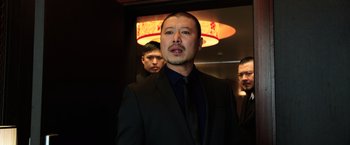 Movie still from “Lucy” (2014), directed by Luc Besson – A man wearing a suit and tie standing next to two other men; Medium shot, Low angle