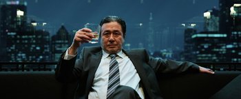 Movie still from “Lucy” (2014), directed by Luc Besson – A man in a suit and tie holding a glass of water; Medium shot, Low angle