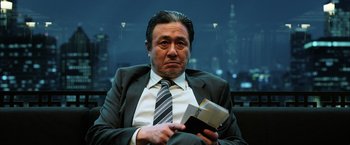 Movie still from “Lucy” (2014), directed by Luc Besson – A man in a suit and tie holding a book; Close Up shot, Low angle