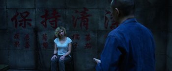 Movie still from “Lucy” (2014), directed by Luc Besson – A woman sitting in front of a man in front of a wall; Medium shot, Over the shoulder angle