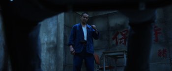 Movie still from “Lucy” (2014), directed by Luc Besson – A man standing in front of a wall holding a camera; Medium shot, Low angle