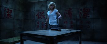 Movie still from “Lucy” (2014), directed by Luc Besson – A woman standing in front of a table holding a sword; Medium shot, Low angle