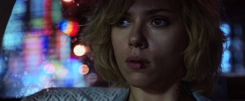 Movie still from “Lucy” (2014), directed by Luc Besson – A woman's face in front of blurry lights at night; Close Up shot, Low angle