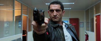 Movie still from “Lucy” (2014), directed by Luc Besson – A man holding a gun in a room; Medium shot, Low angle