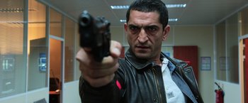 Movie still from “Lucy” (2014), directed by Luc Besson – A man holding a gun in a room; Close Up shot, Low angle