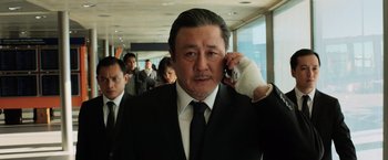 Movie still from “Lucy” (2014), directed by Luc Besson – A man in a suit and tie talking on a cell phone; Close Up shot, Low angle