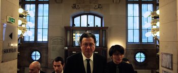 Movie still from “Lucy” (2014), directed by Luc Besson – A man standing next to two other men in a suit; Medium shot, Low angle