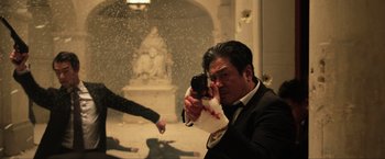 Movie still from “Lucy” (2014), directed by Luc Besson – A man holding a cell phone in front of a statue; Medium shot, Low angle