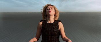 Movie still from “Lucy” (2014), directed by Luc Besson – A woman in a black dress standing in the middle of a road; Medium shot, Low angle