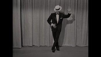 Movie still from “Lucy and Desi” (2022), directed by Amy Poehler – A man in a suit and hat is waving; Wide shot, High angle