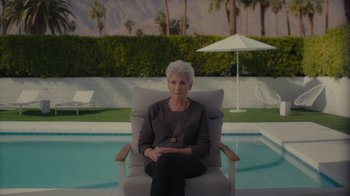 Movie still from “Lucy and Desi” (2022), directed by Amy Poehler – An older woman sitting in a chair near a pool; Wide shot, Low angle