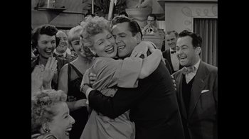Movie still from “Lucy and Desi” (2022), directed by Amy Poehler – A man and a woman hugging each other in front of a crowd; Medium shot, Over the shoulder angle