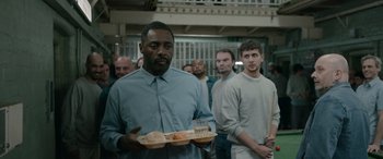 Movie still from “Luther: The Fallen Sun” (2023), directed by Jamie Payne – A group of people standing around a building; Medium shot, Over the shoulder angle