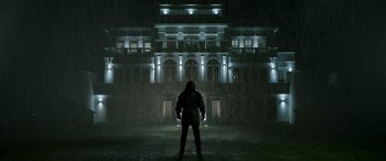 Movie still from “Luther: The Fallen Sun” (2023), directed by Jamie Payne – A man standing in the rain in front of a large building; Wide shot, Low angle