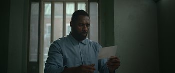 Movie still from “Luther: The Fallen Sun” (2023), directed by Jamie Payne – A man holding a piece of paper in front of a window; Close Up shot, High angle