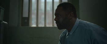 Movie still from “Luther: The Fallen Sun” (2023), directed by Jamie Payne – A man with a beard is sitting in front of a window; Close Up shot, Over the shoulder angle
