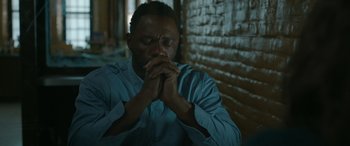 Movie still from “Luther: The Fallen Sun” (2023), directed by Jamie Payne – A man sitting in front of a brick wall with his eyes closed; Close Up shot, High angle