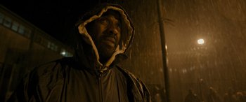 Movie still from “Luther: The Fallen Sun” (2023), directed by Jamie Payne – A man in a hooded jacket standing in the pouring rain; Close Up shot, Low angle