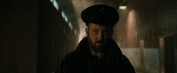 Movie still from “Luther: The Fallen Sun” (2023), directed by Jamie Payne – A man with a beard wearing a hat and standing in the rain; Close Up shot, Low angle