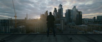 Movie still from “Luther: The Fallen Sun” (2023), directed by Jamie Payne – A man standing on a ledge looking out at a city skyline; Extreme Wide shot, Low angle