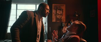 Movie still from “Luther: The Fallen Sun” (2023), directed by Jamie Payne – A man in a suit and tie talking to another man in a suit and tie; Medium shot, Over the shoulder angle