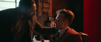Movie still from “Luther: The Fallen Sun” (2023), directed by Jamie Payne – A man getting his hair cut by another man; Close Up shot, Over the shoulder angle