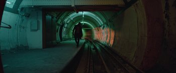 Movie still from “Luther: The Fallen Sun” (2023), directed by Jamie Payne – A person is walking in a tunnel near a train tracks; Wide shot, High angle