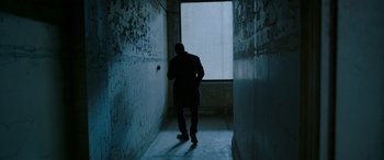 Movie still from “Luther: The Fallen Sun” (2023), directed by Jamie Payne – A man standing in a dark hallway looking out a window; Wide shot, High angle