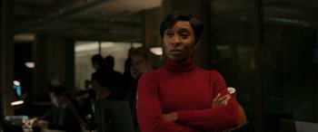 Movie still from “Luther: The Fallen Sun” (2023), directed by Jamie Payne – A woman in a red sweater is standing with her arms crossed; Medium shot, Over the shoulder angle