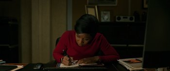 Movie still from “Luther: The Fallen Sun” (2023), directed by Jamie Payne – A woman is writing in a notebook at a table; Medium shot, High angle