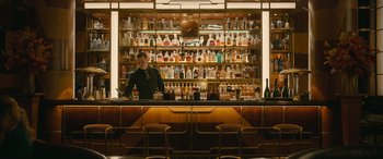 Movie still from “Luther: The Fallen Sun” (2023), directed by Jamie Payne – A man standing behind a bar in front of many bottles; Wide shot, High angle