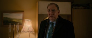 Movie still from “Luther: The Fallen Sun” (2023), directed by Jamie Payne – An older man wearing a suit and tie; Close Up shot, Over the shoulder angle