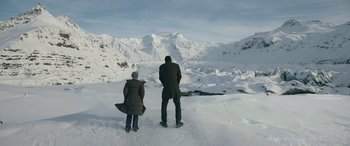 Movie still from “Luther: The Fallen Sun” (2023), directed by Jamie Payne – A man and a woman standing in the snow looking at a mountain; Extreme Wide shot, High angle