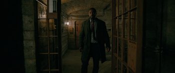 Movie still from “Luther: The Fallen Sun” (2023), directed by Jamie Payne – A man in a coat and tie walking in a room; Wide shot, Low angle