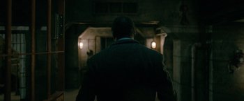 Movie still from “Luther: The Fallen Sun” (2023), directed by Jamie Payne – A man standing in a dark room looking at a building; Medium shot, Over the shoulder angle